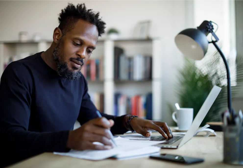 A man writing on paper while working on his laptop
